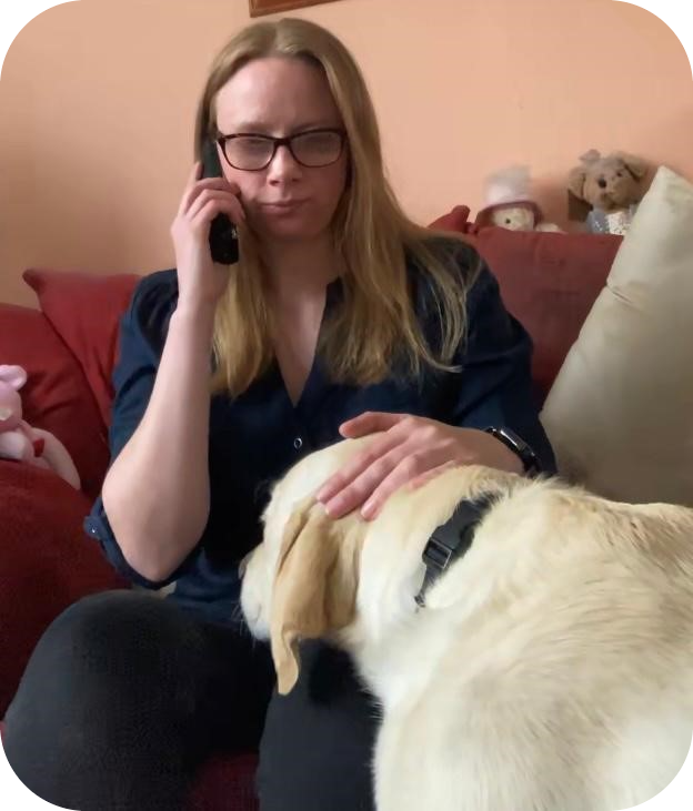 A photo of a lady on the phone receiving telephone counselling, she has her guide dog by her side.